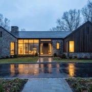 Modern stone and wood luxury home in Bergen County, New Jersey at dusk with interior lights glowing