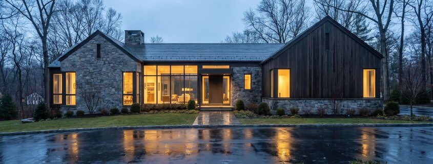 Modern stone and wood luxury home in Bergen County, New Jersey at dusk with interior lights glowing